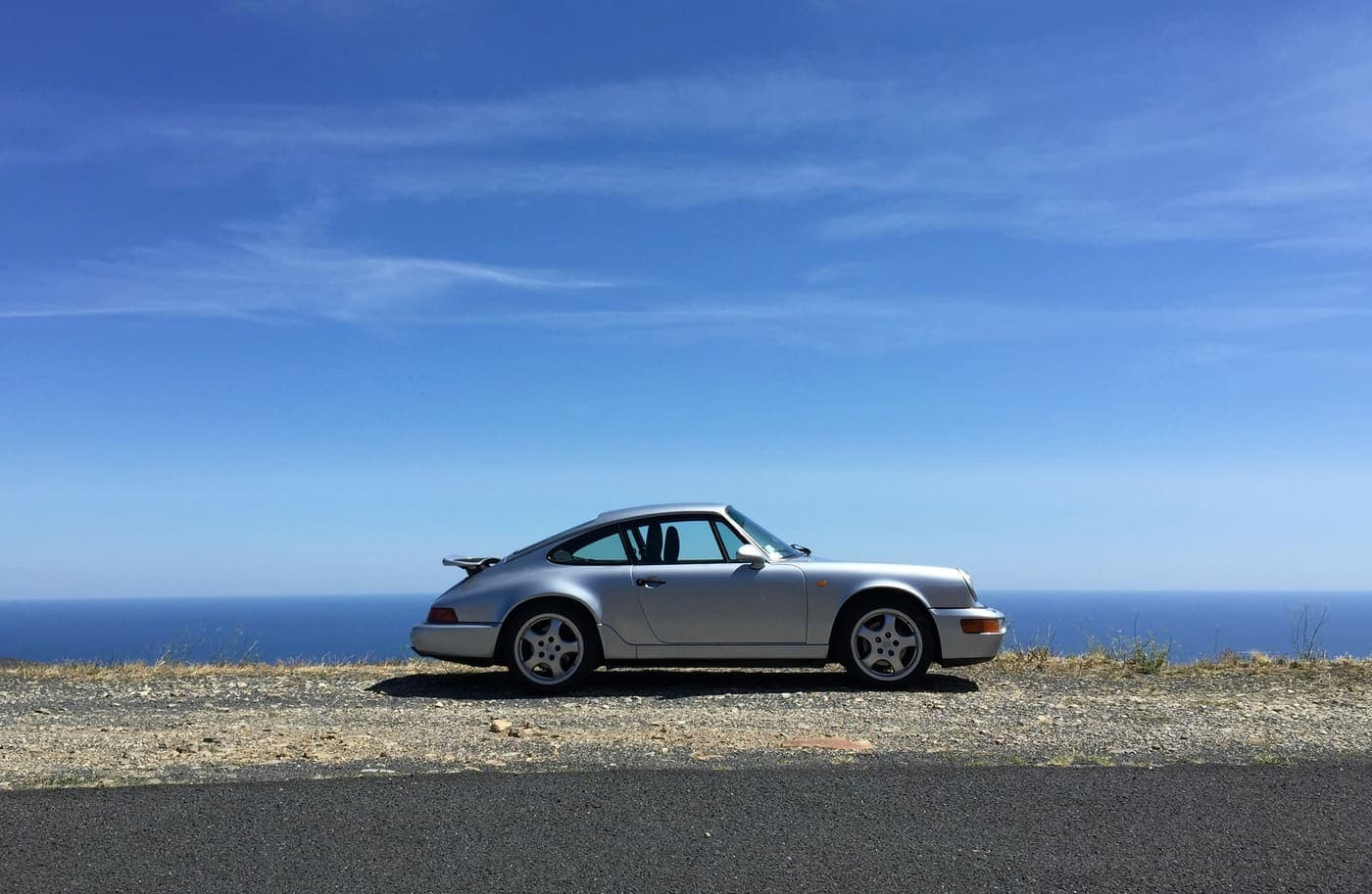 A silver classic coupe parked on a clifftop above the sea