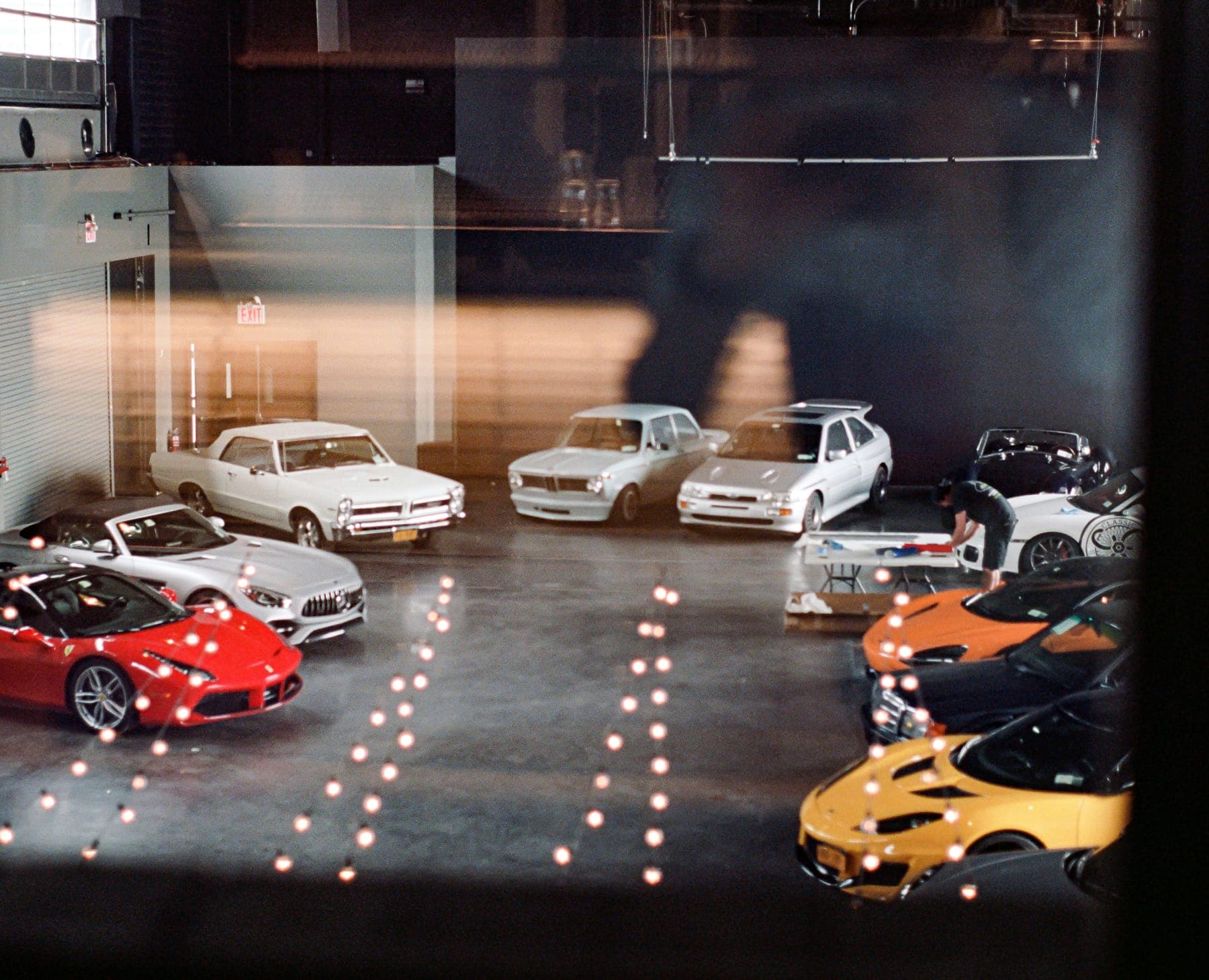 Classic and modern cars parked around an indoor garage, seen from above through a window